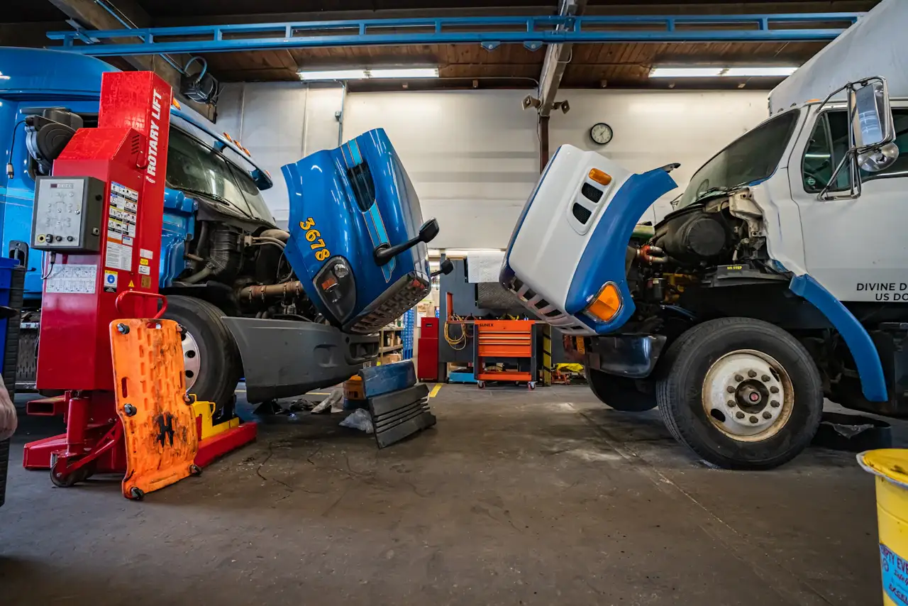 Truck breakdown repair service in a heavy-duty shop with two commercial trucks undergoing diagnostics and mechanical repairs with hoods raised.