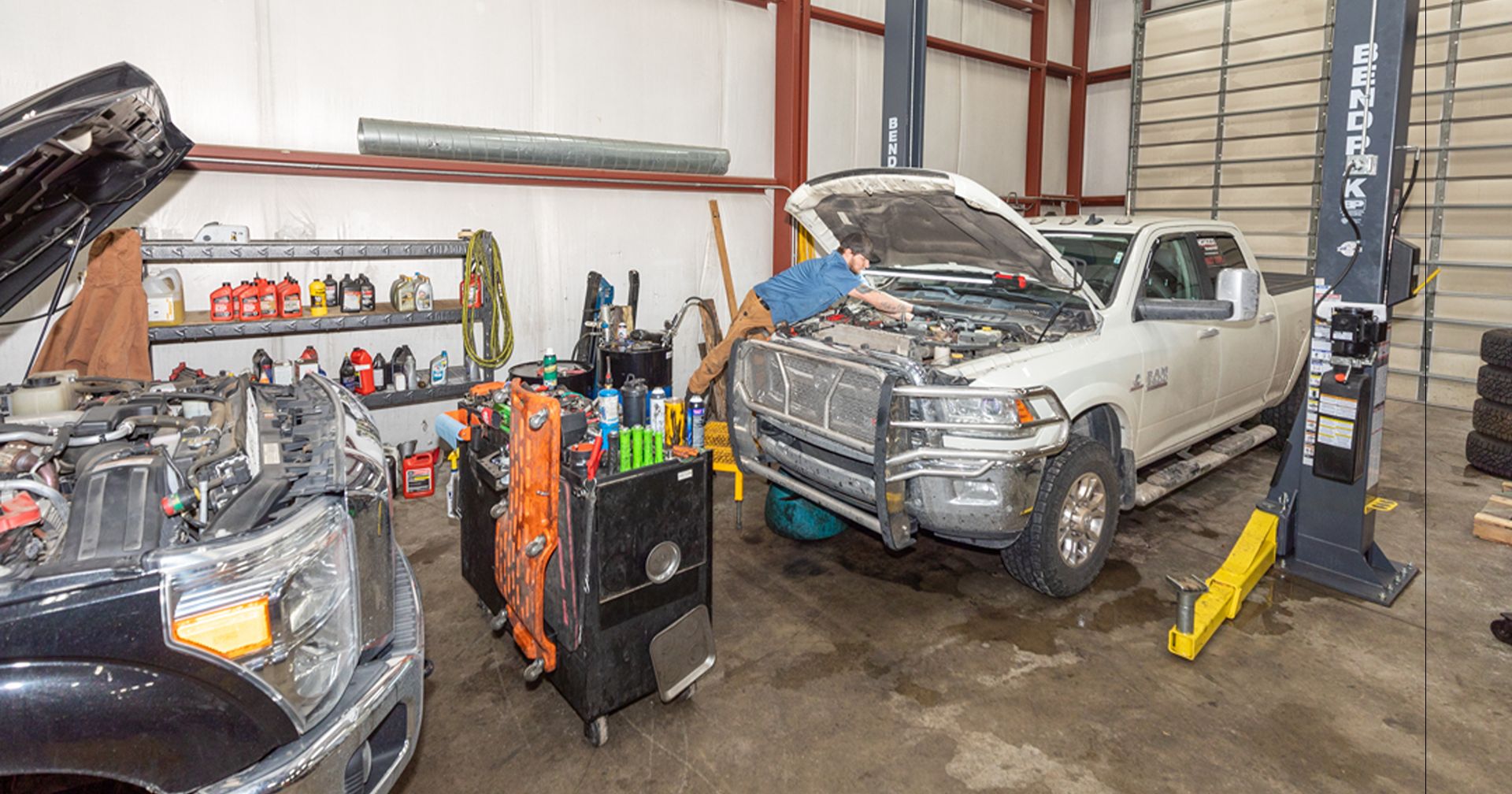Mechanic performs light-duty repair under the hood of a RAM 3500 pickup in a fully equipped service bay.