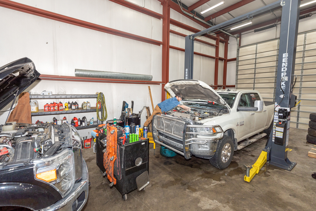 Mechanic performs light-duty repair under the hood of a RAM 3500 pickup in a fully equipped service bay.