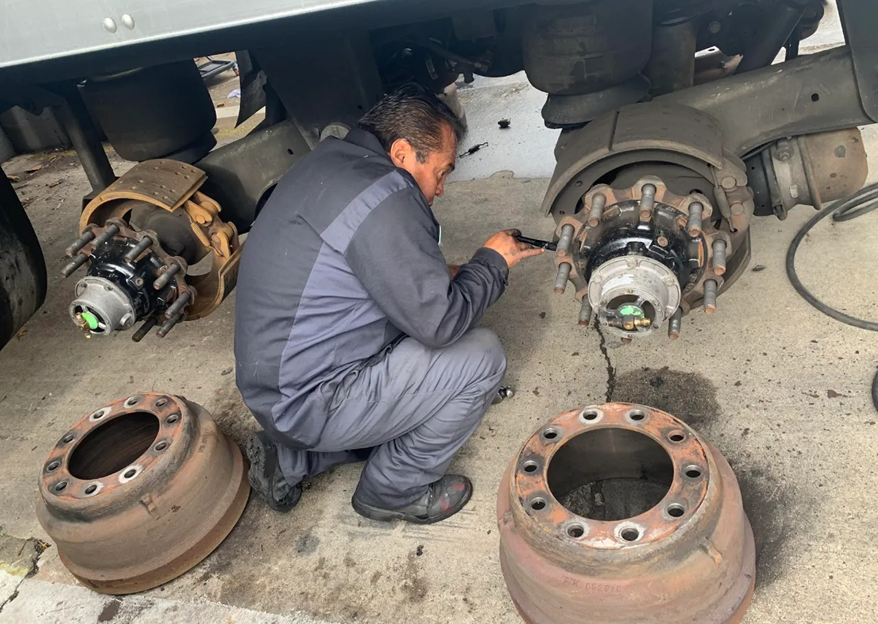 Heavy-duty brake repair technician servicing a truck wheel hub with the brake drums removed.