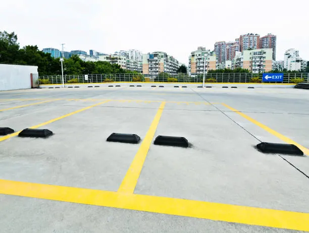 Fotografía de un estacionamiento al aire libre completamente vacío donde se observan claramente los topes de estacionamiento en cada cajón