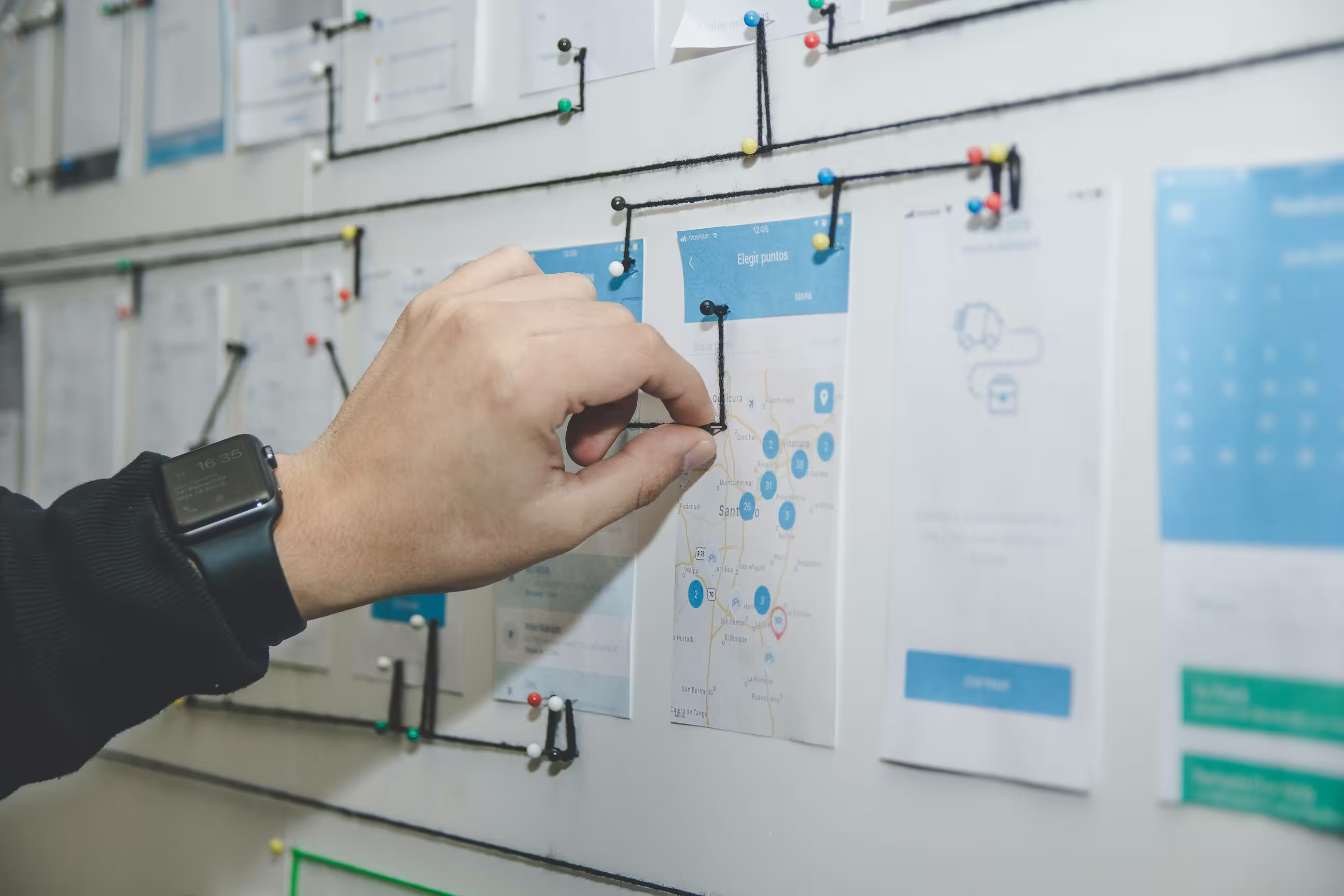 Hand arranging printed app screens with pins and string on a design board