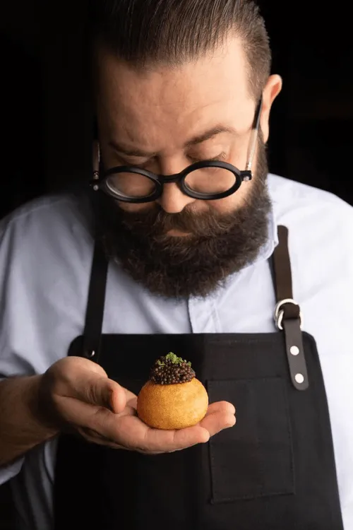 A man with a beard and glasses holding a pastry.