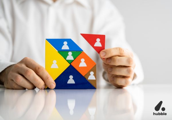 Person holding a red puzzle piece with a user icon, fitting it into a colorful structure representing team hierarchy and employee management.