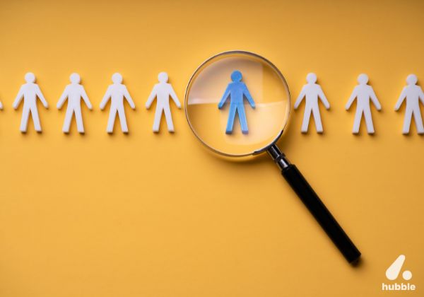 Magnifying glass highlighting a blue figure among white cutouts, symbolizing AI-driven employee recognition.