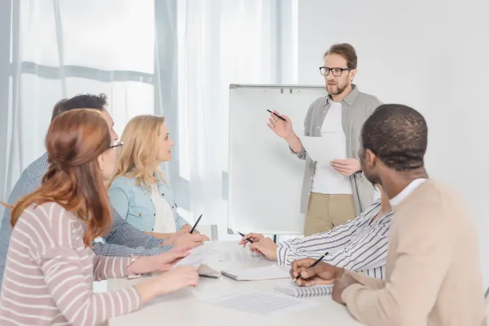 Un formateur présente un cours à un petit groupe d’adultes attentifs autour d’une table, lors d’une formation en investissement immobilier locatif.