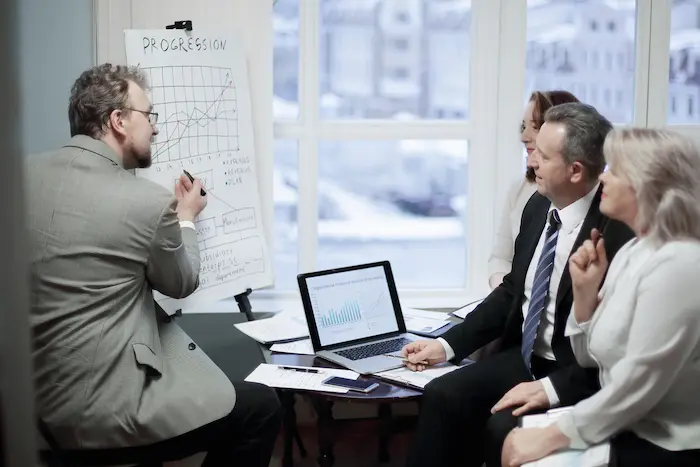 Un formateur en investissement immobilier anime une session de formation devant trois participants attentifs, dans une salle lumineuse et professionnelle.