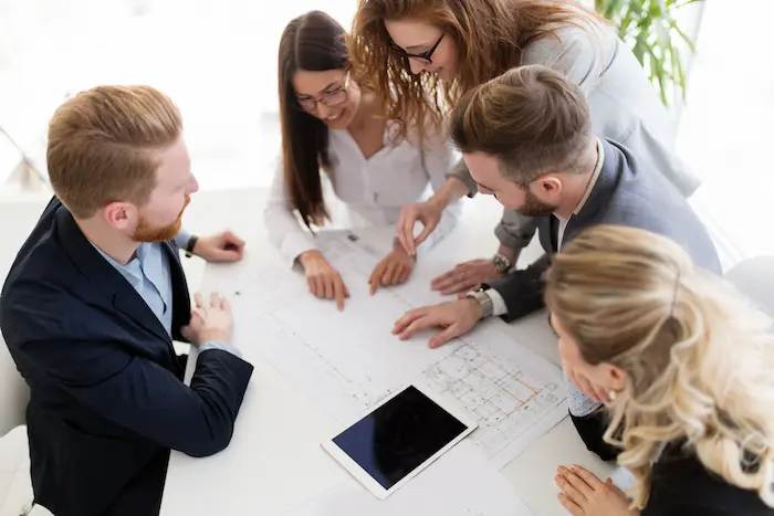 Un groupe de professionnels souriants et attentifs, penchés sur des plans, apprenant et discutant de stratégies d'investissement immobilier.