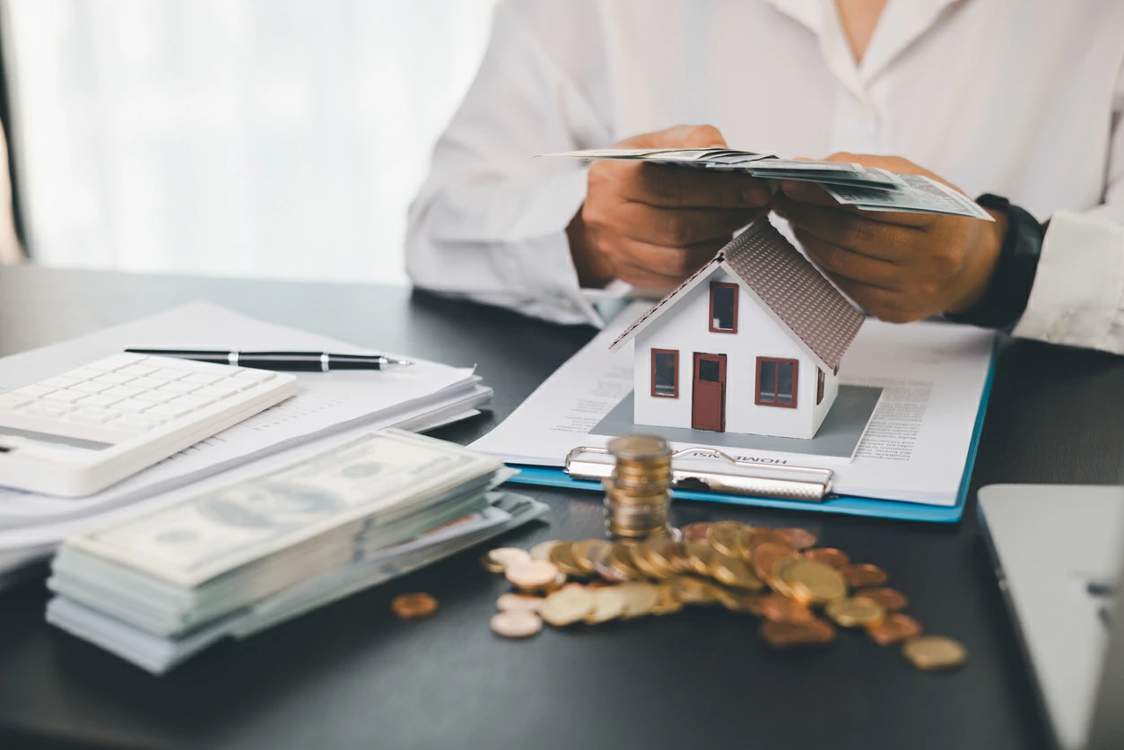 Homme tenant des liasses de billets au-dessus d'une petite maison.