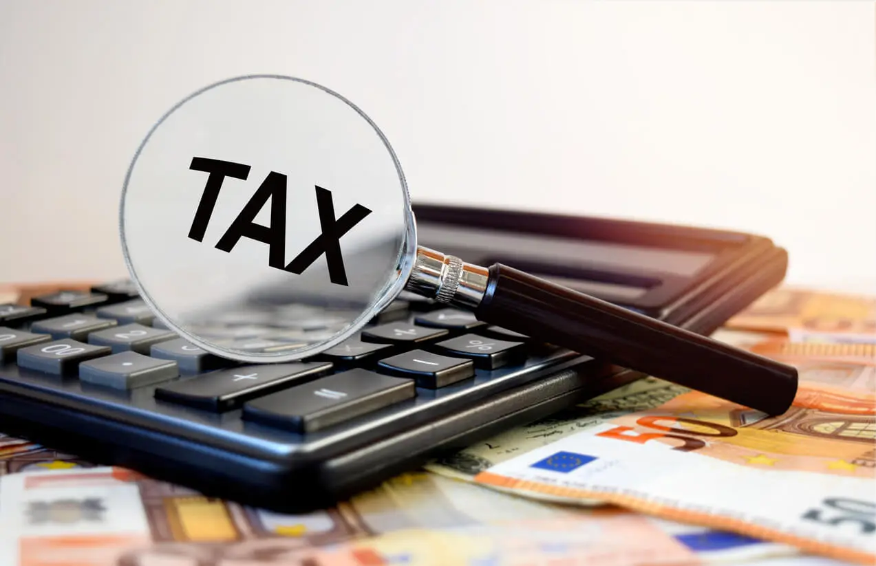 Mot tax dans une loupe posée au-dessus d'une calculatrice et des liasses de billets en euro.