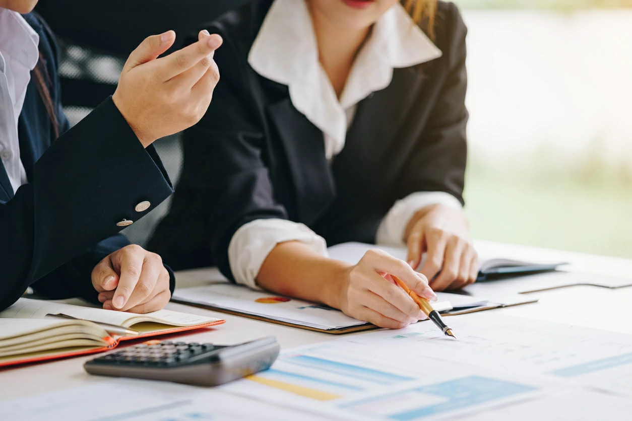 Deux femmes consultant des documents chiffrés à côté d'autre documents et une calculatrice.