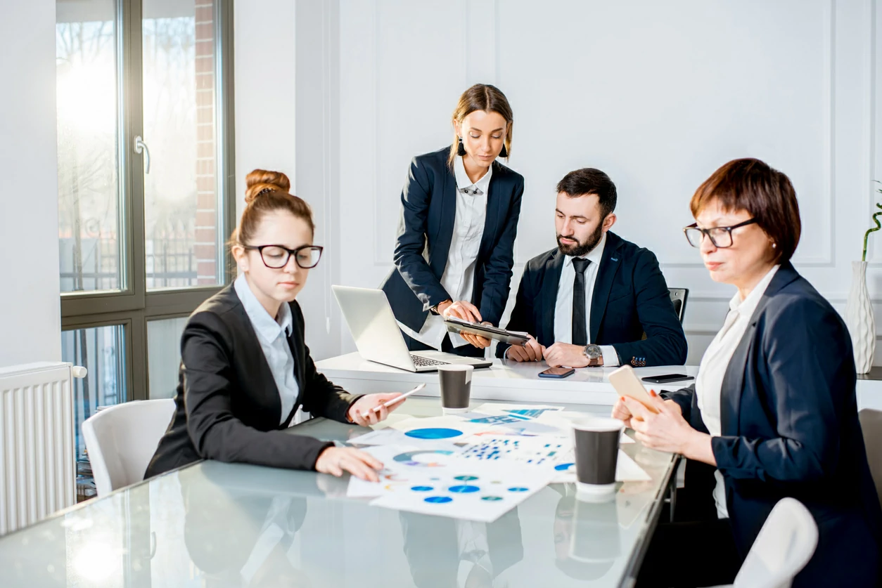 Quatre personnes consultant divers documents autour d'une table longue.