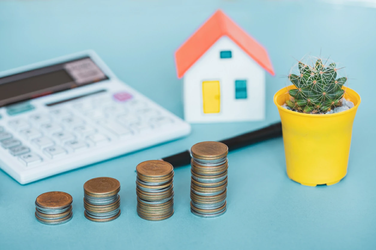 Quatre piles  de pièces de monnaie, une calculatrice; un pot de fleurs et une petite maison.