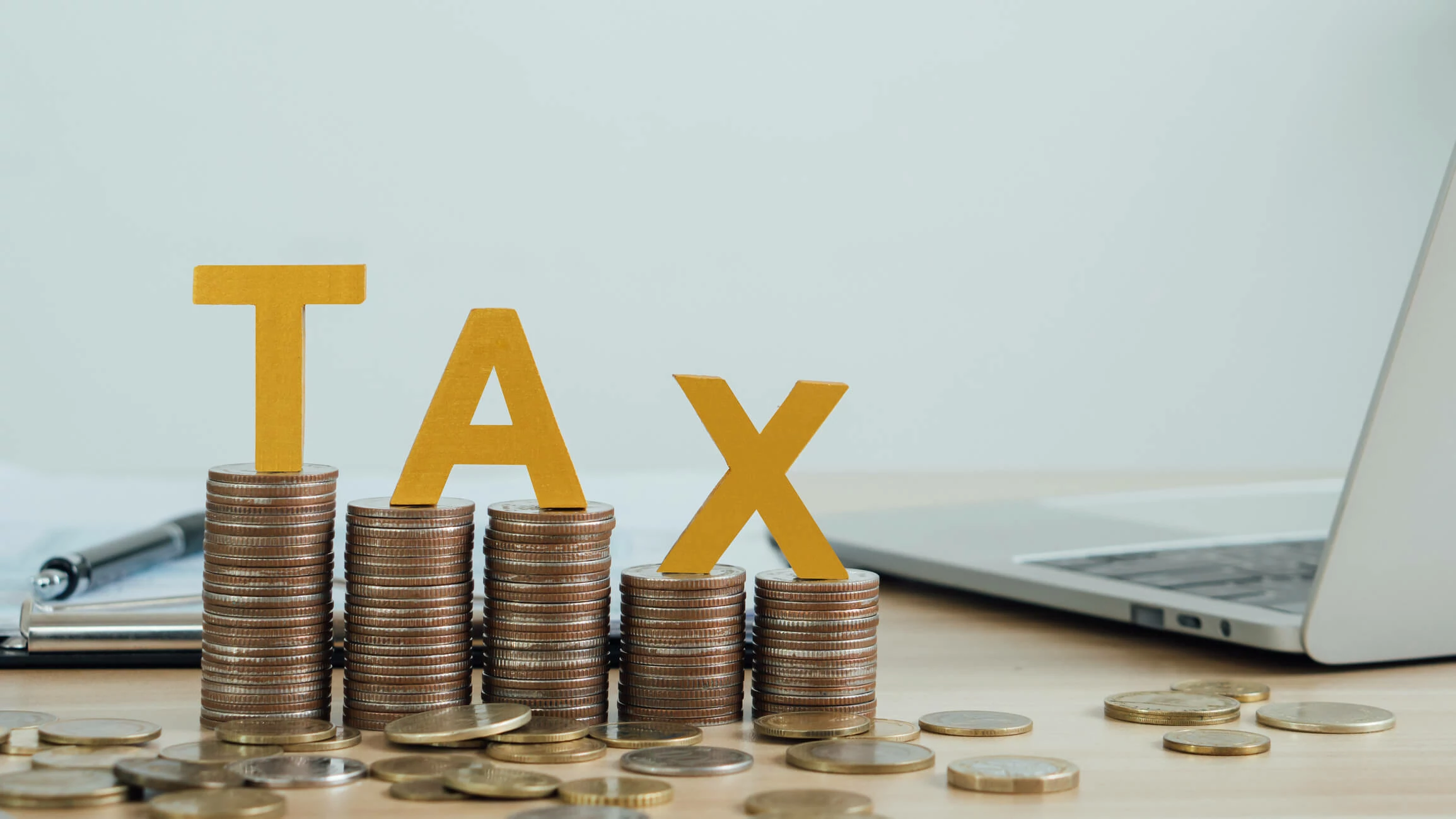 Pièces de monnaie éparpillées, le mot taxe et un ordinateur portable.