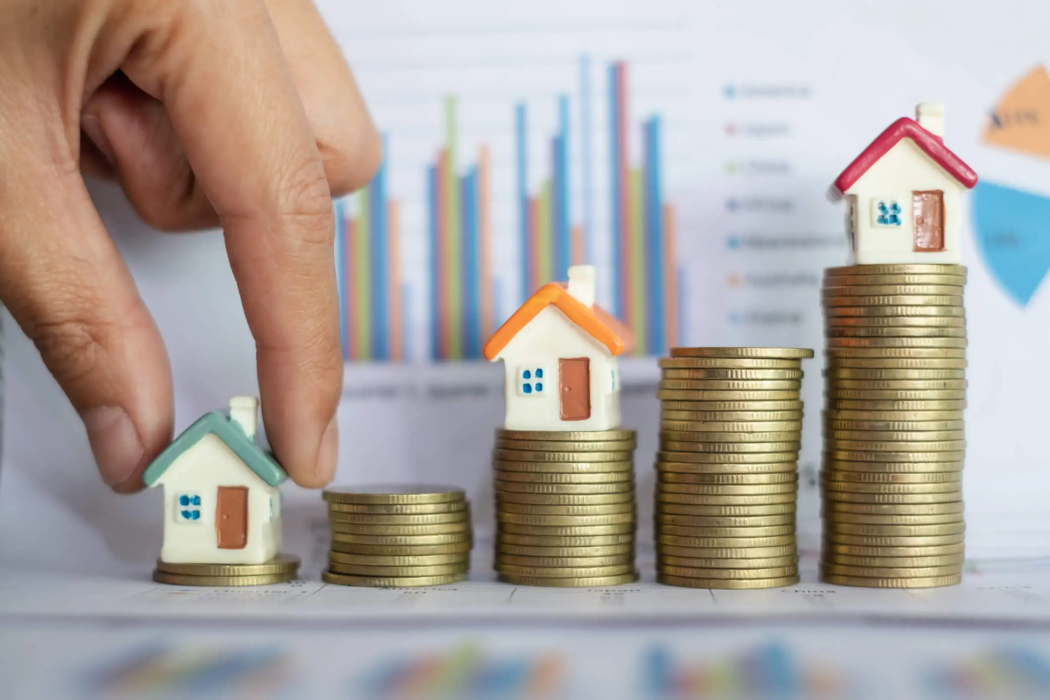 Main posant une maison miniature sur des piles de pièces de monnaie.