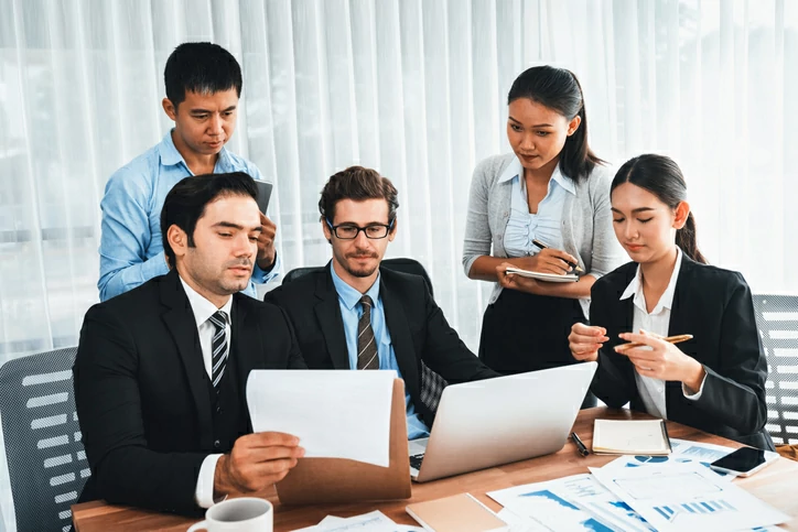 5 personnes autour d'une table avec des documents et un ordinateur portable.
