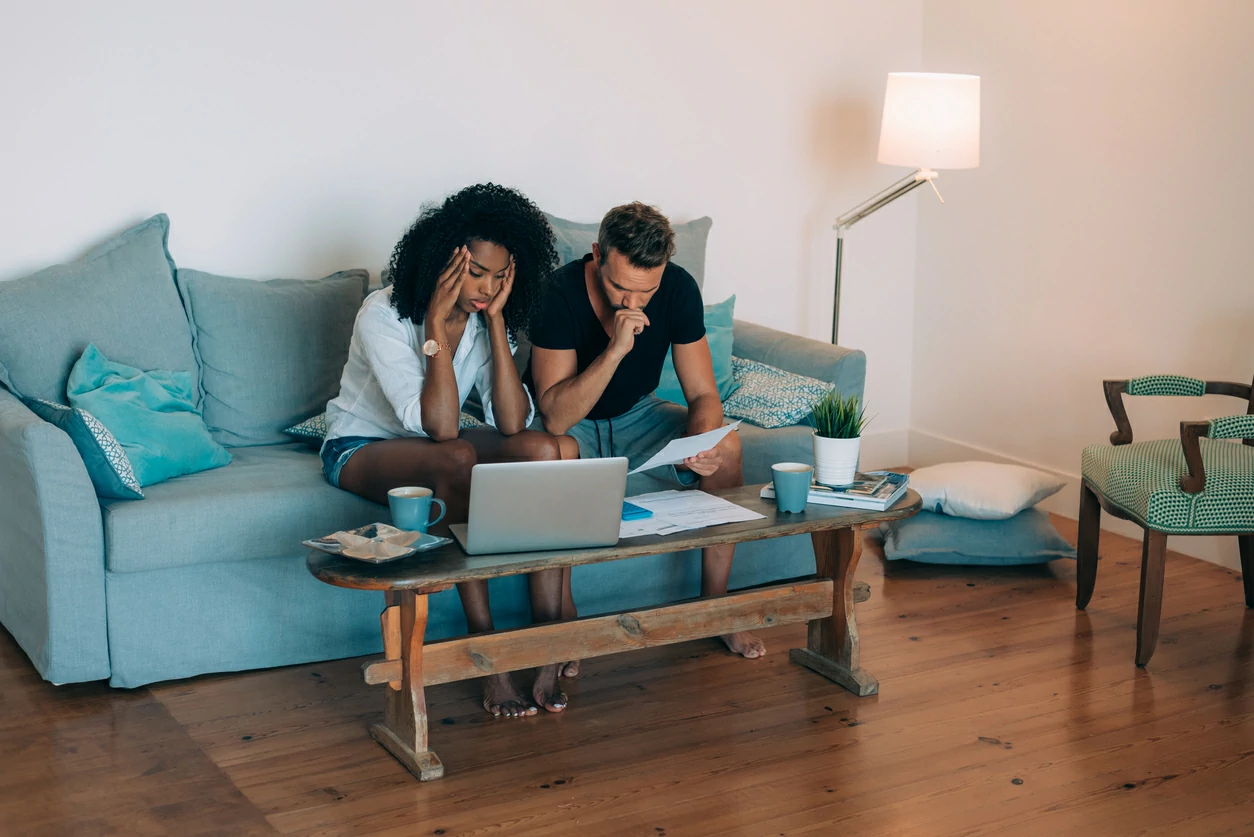 Un homme et une femme contrariés devant des documents et un ordinateur portable.
