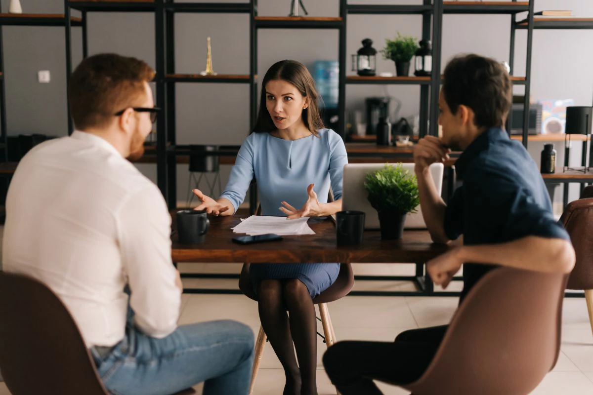 Femme en pleine explication devant deux hommes autour d'une table.