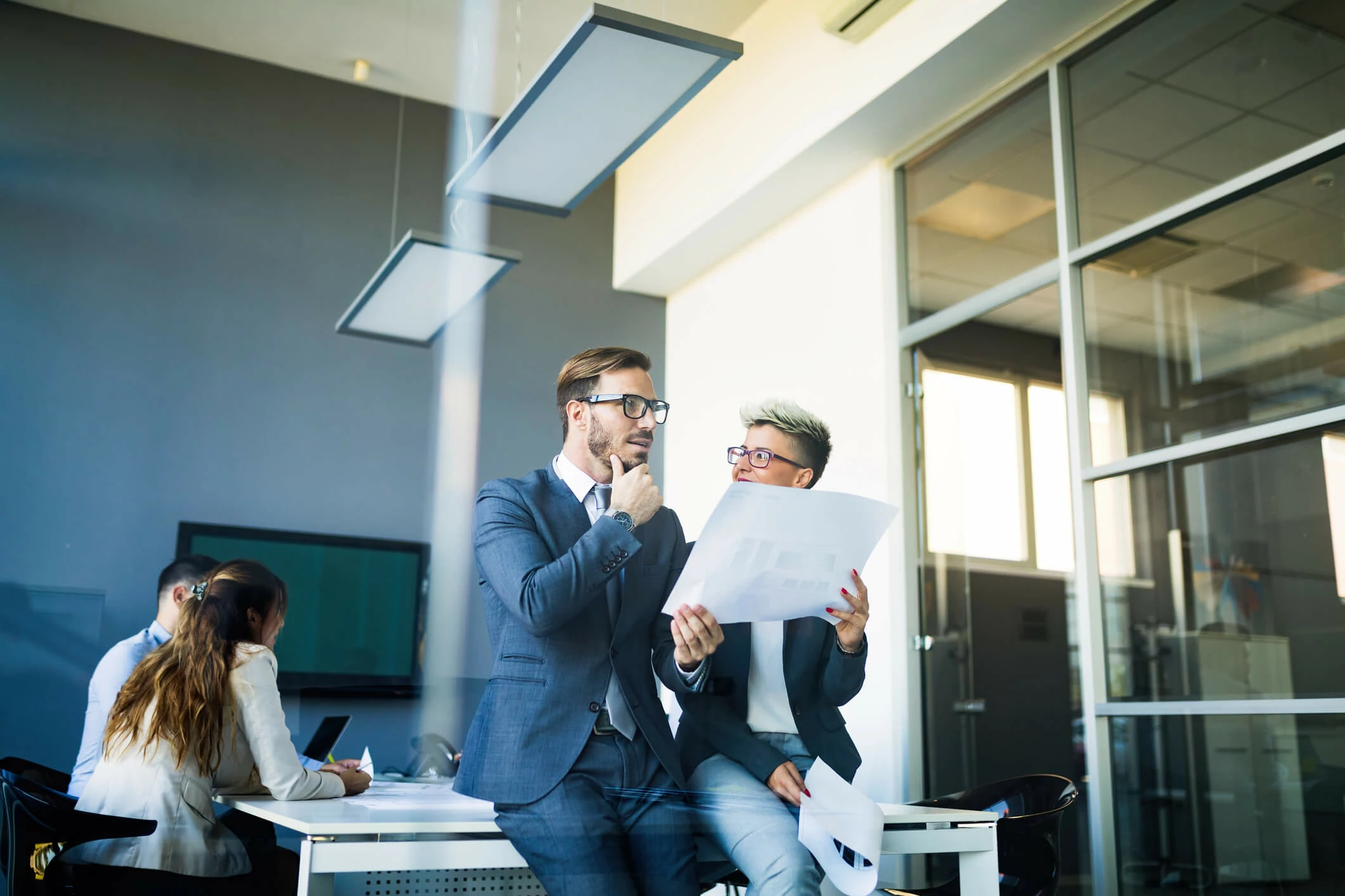 Deux personnes assises au coin d'une table consultant un document dans une salle de réunion.