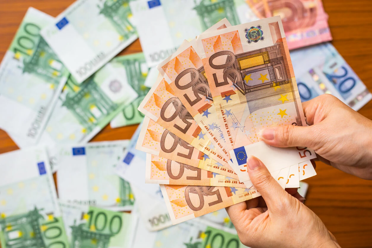 Main tenant plusieurs billets de 50 euros et plusieurs billets éparpillés en arrière-plan.