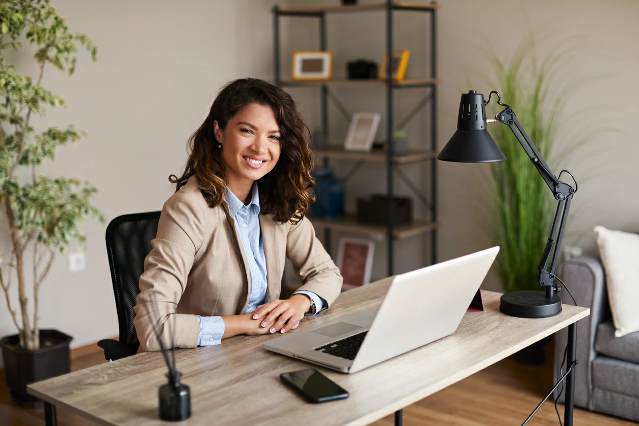 Femme en costard devant un bureau avec un ordinateur portable et des documents.