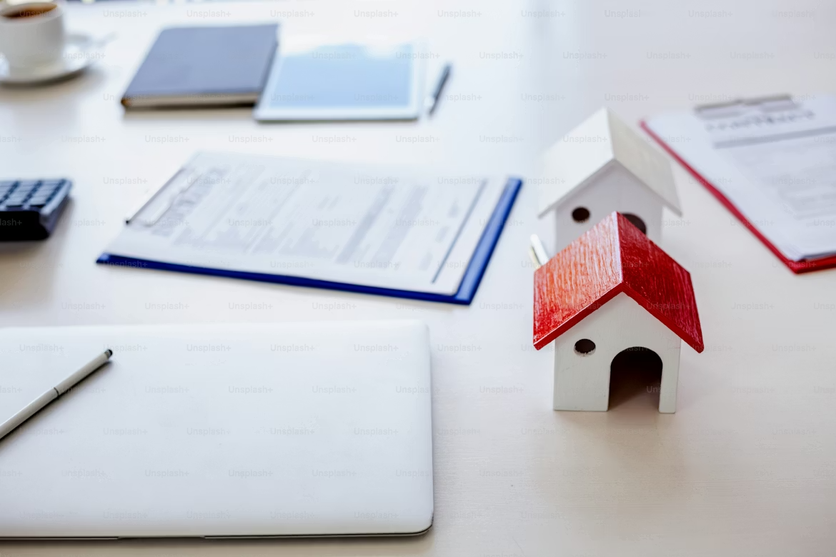 Deux petites maison en bois, des documents éparpillés et un ordinateur portable fermé.