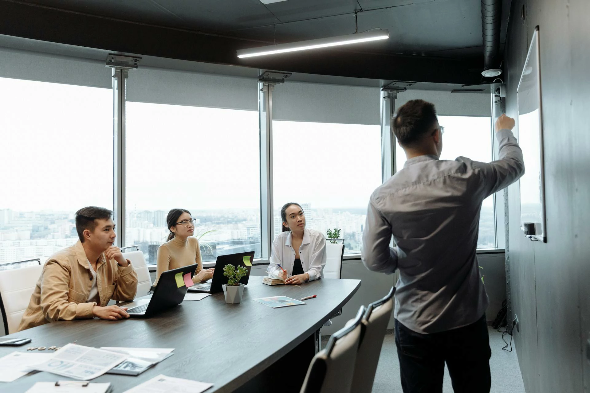 Un formateur devant un tableau blanc et trois personnes assises avec des ordinateurs portables en face.