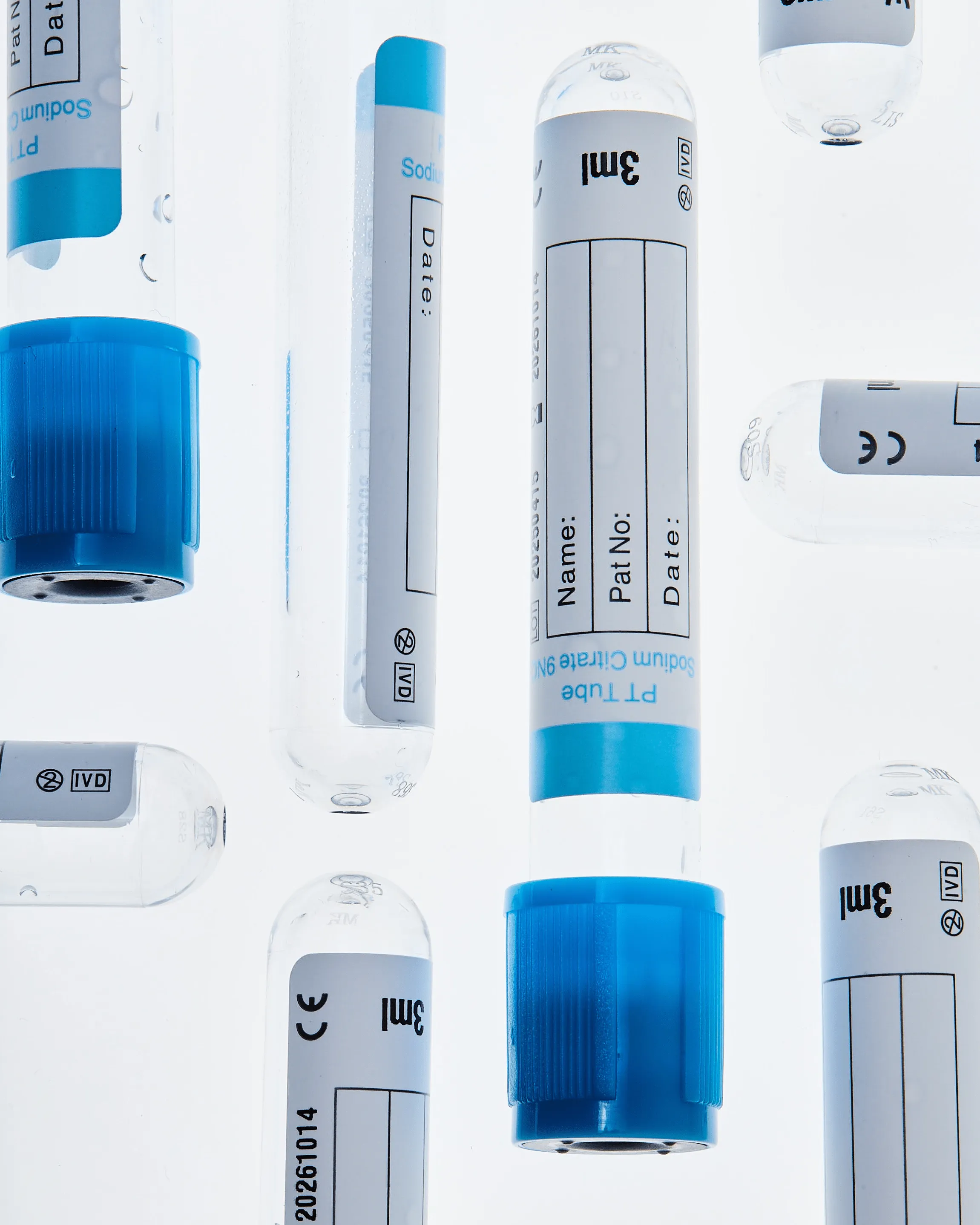 Multiple clear medical sample tubes with blue caps and white labels showing patient information fields, floating on a white background.