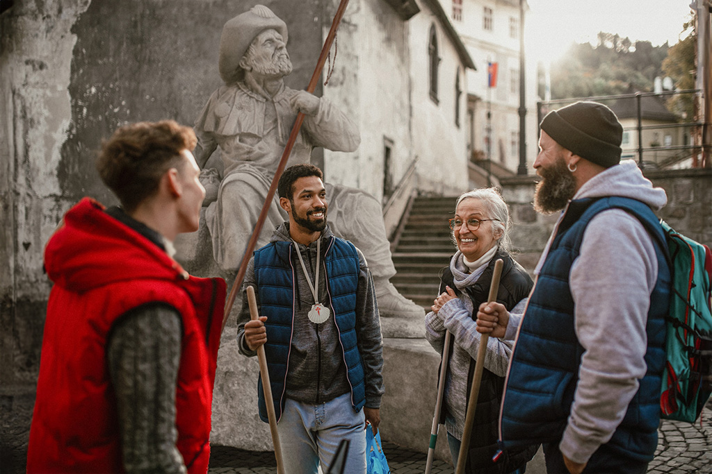 Un grupo variado de peregrinos conversando delante de la escultura de Santiago. 