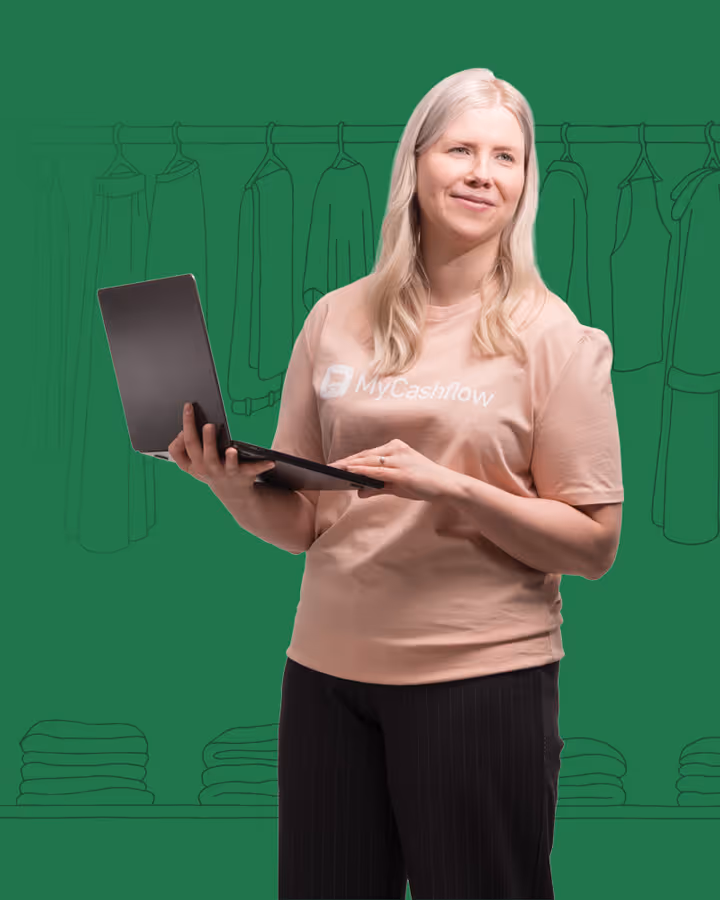 Nainen työskentelee kannettavalla tietokoneella MyCashflow-paita päällä vihreää taustaa vasten.