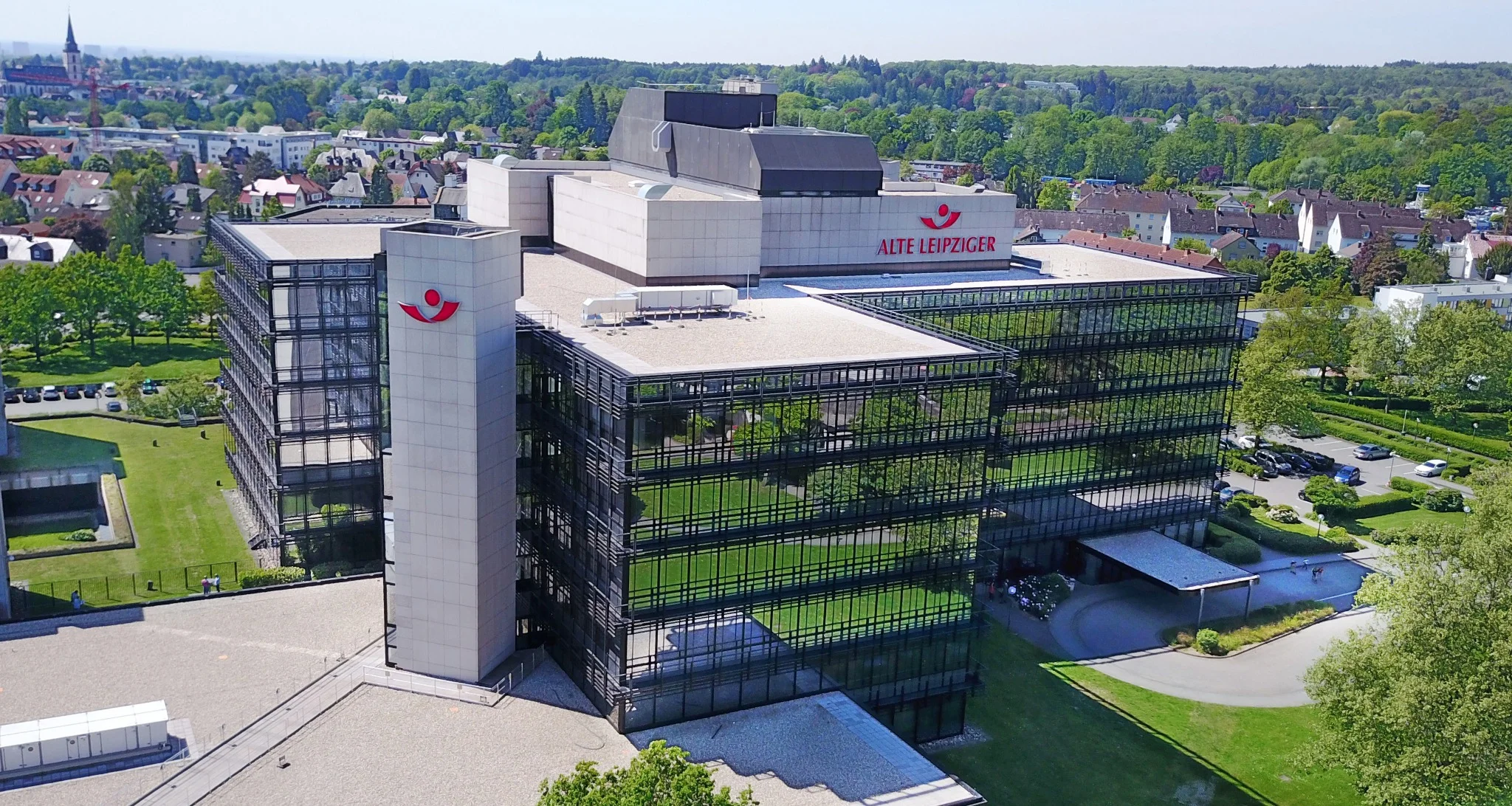 Luftaufnahme eines modernen Bürogebäudes mit Glasfassade und angrenzenden Grünflächen in einem Gewerbegebiet