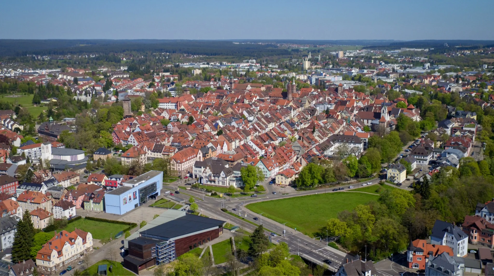 Luftaufnahme einer Kleinstadt mit dichter Wohnbebauung, roten Ziegeldächern, Grünflächen und umliegender Landschaft