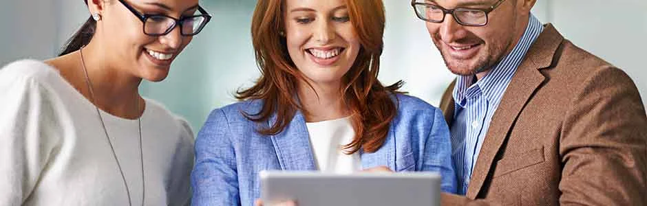 Three people look at a tablet together and smile