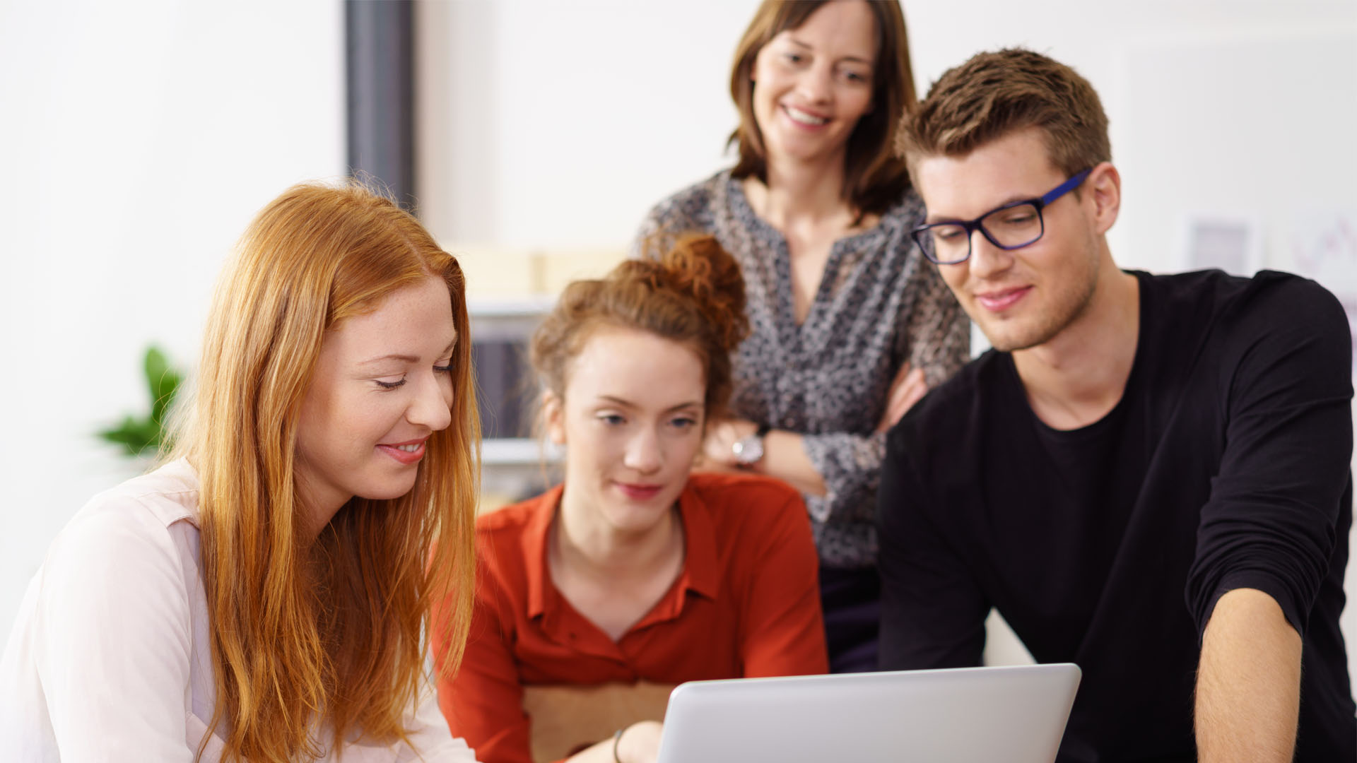 Four colleagues are working together on a laptop in the office and discussing a project as a team