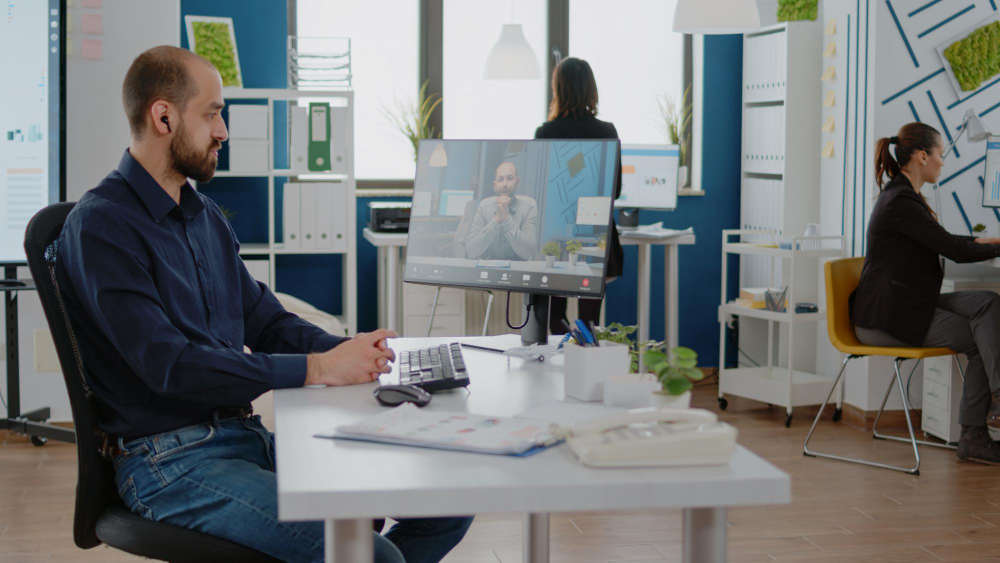A man is sitting at his hybrid workspace, thereby practicing workplace sharing.