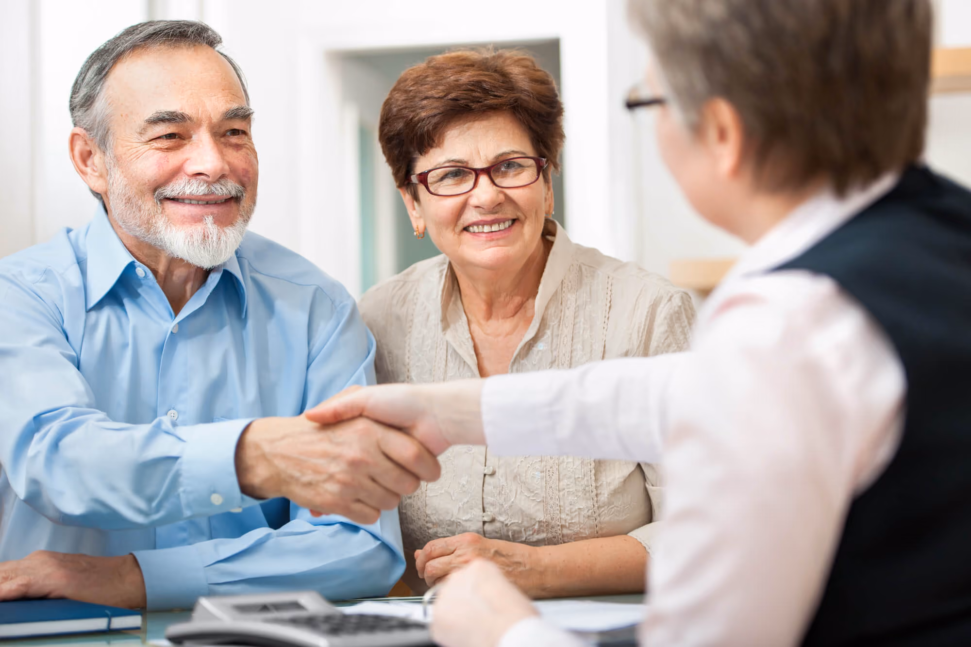a man and a woman shaking hands over a table while a woman next to the man smiles