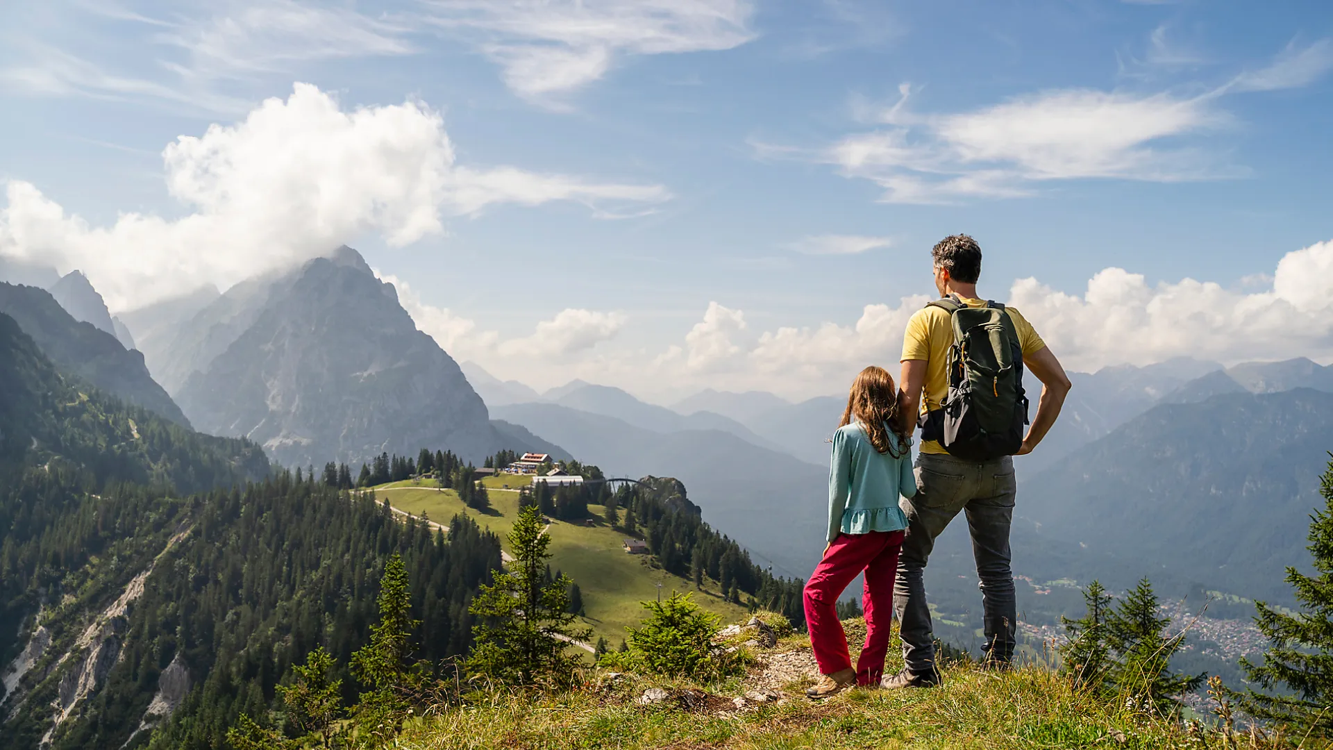 Familie wandert gemeinsam auf einem Panorama-Bergweg mit weiter Aussicht