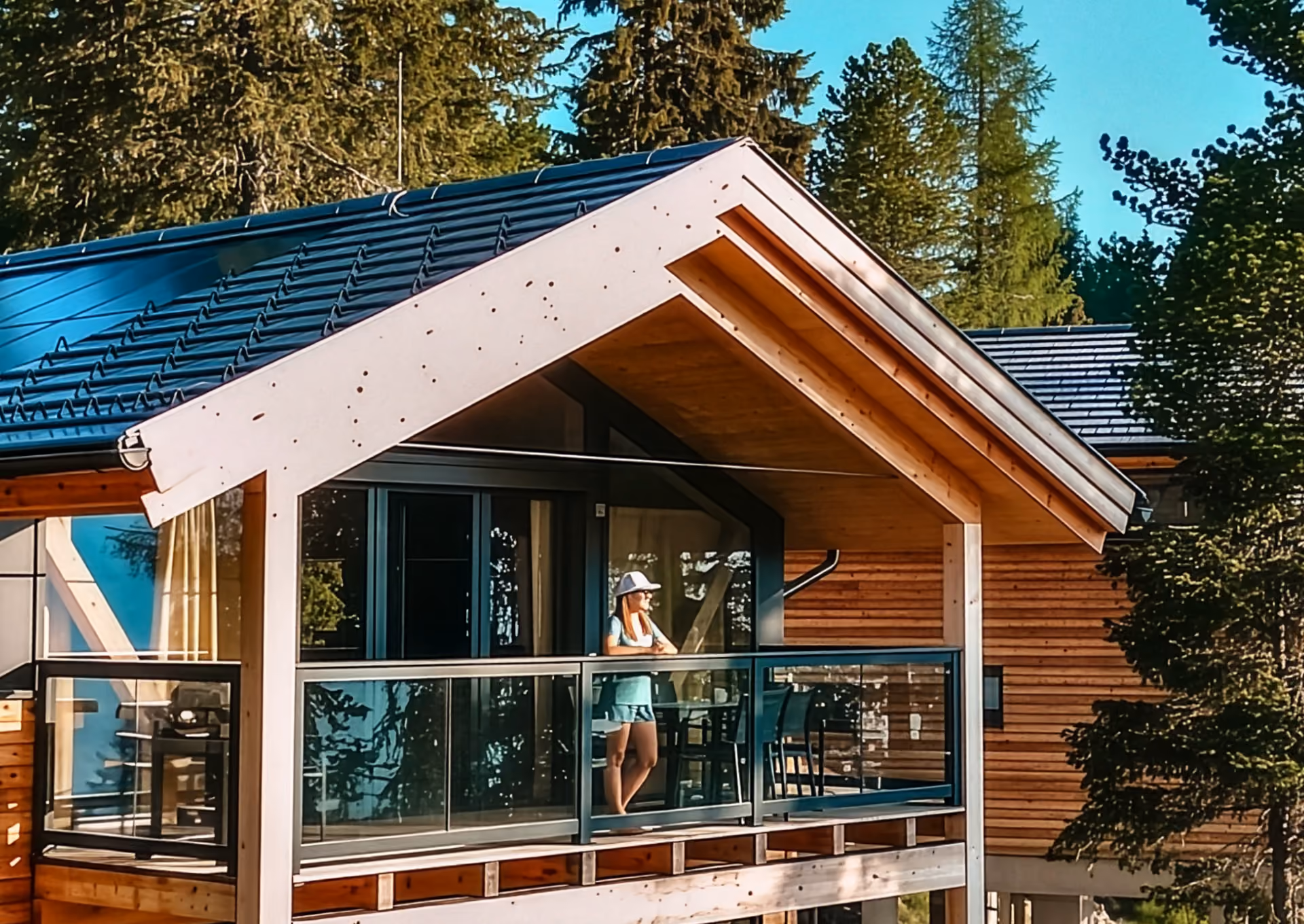 Modernes Holzchalet in Österreich mit großzügigem Glasbalkon und Blick in den Bergwald – ALMDORFBAU Ferienimmobilie