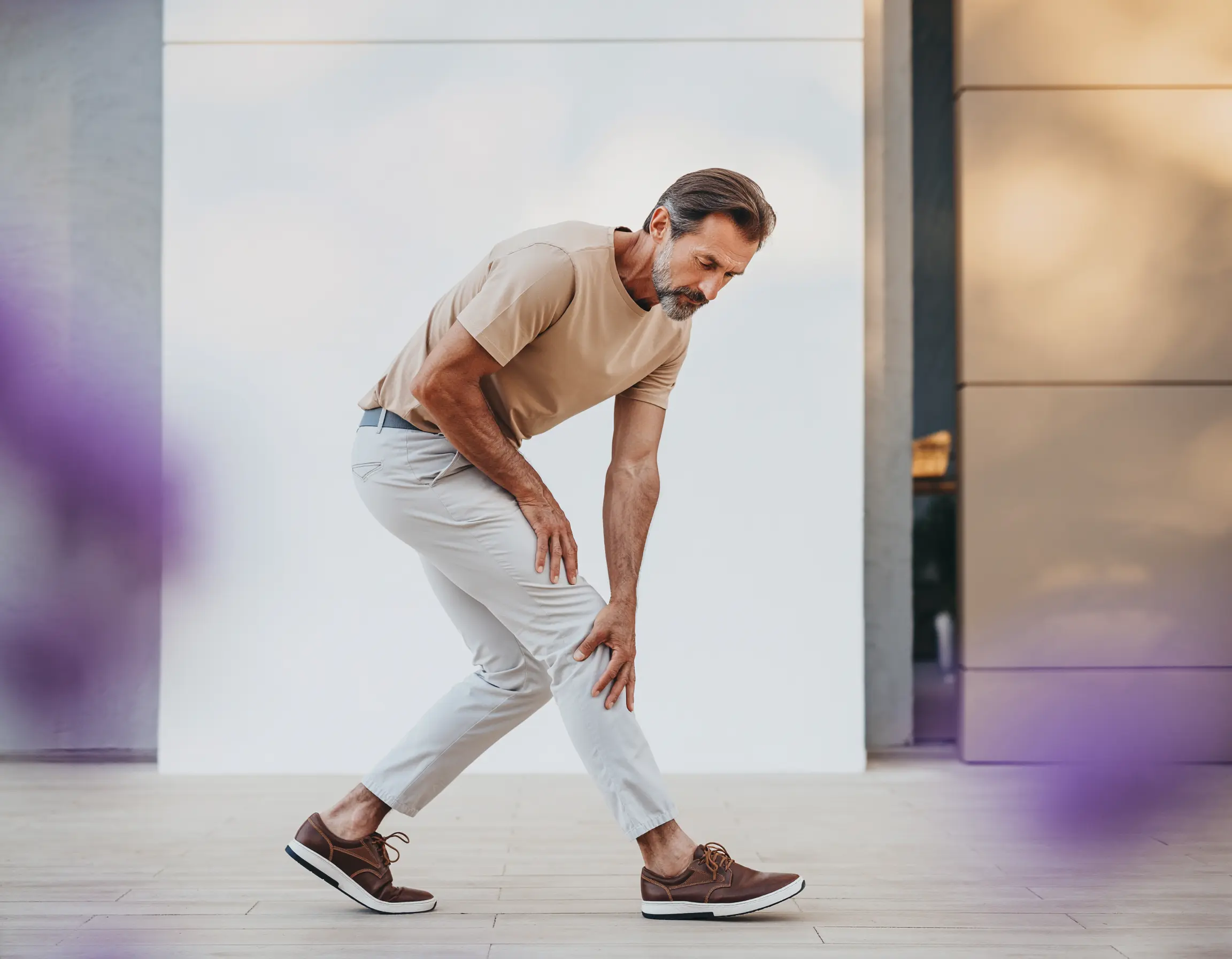 Middle-aged man bending forward and holding his right knee, showing discomfort or pain.