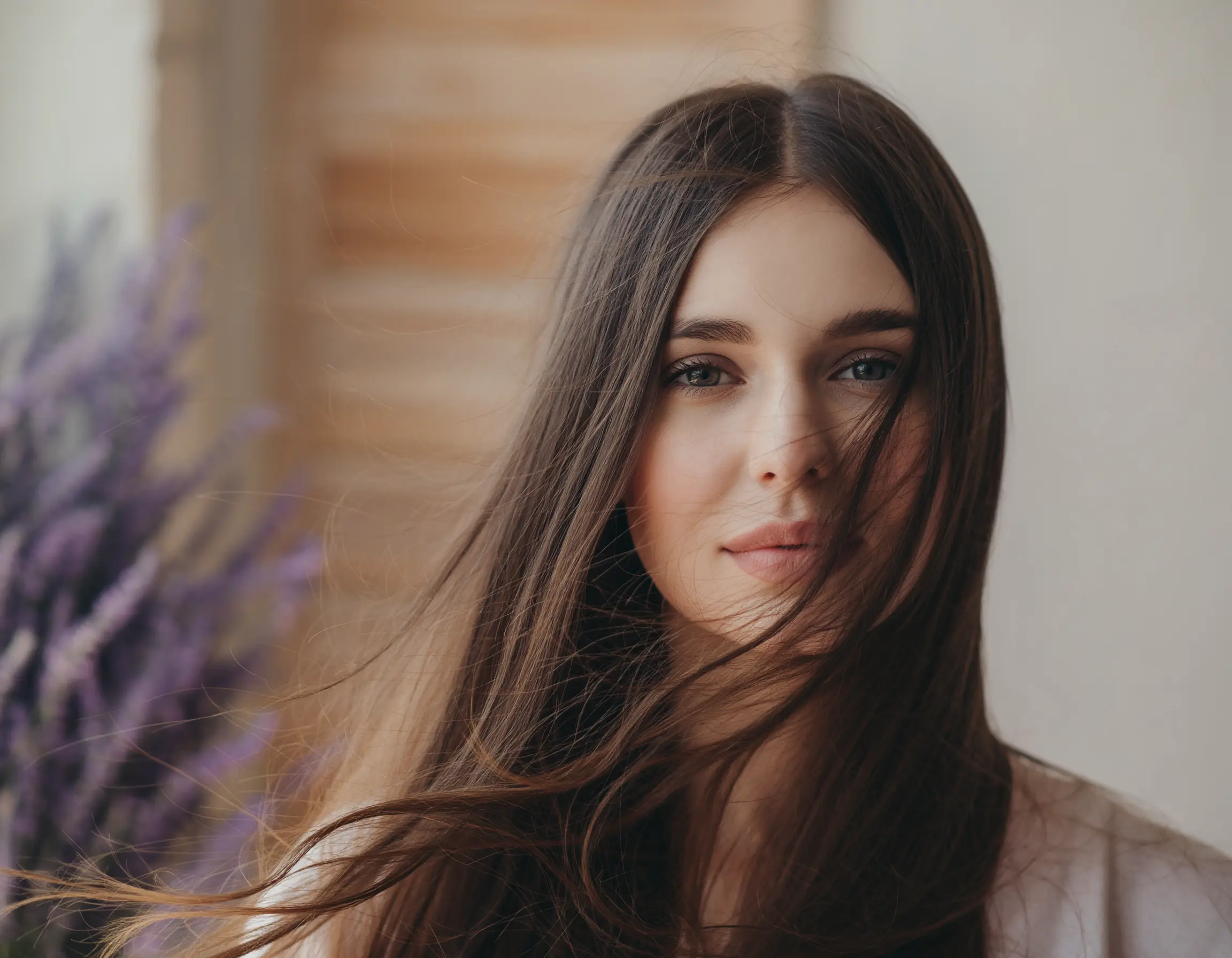 Close-up of a young woman with long brown hair partially covering her face, looking directly at the camera with a soft smile.