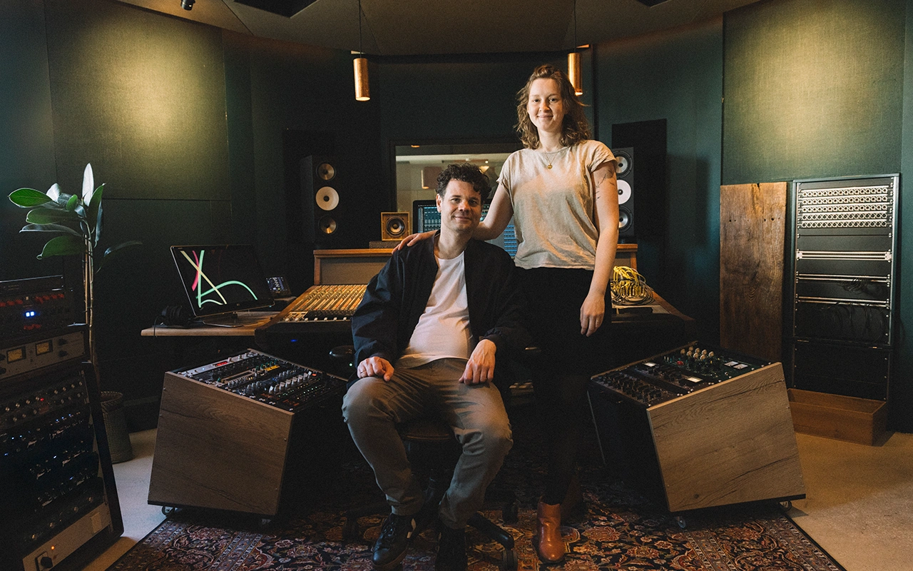 Zwei Selbstständige lächeln in ihrem Tonstudio zwischen Mischpulten und Studiotechnik.