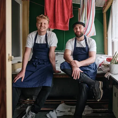 Die Gründer des Restaurants Hawara sitzen lächelnd in ihren Schürzen in ihrem Lokal.