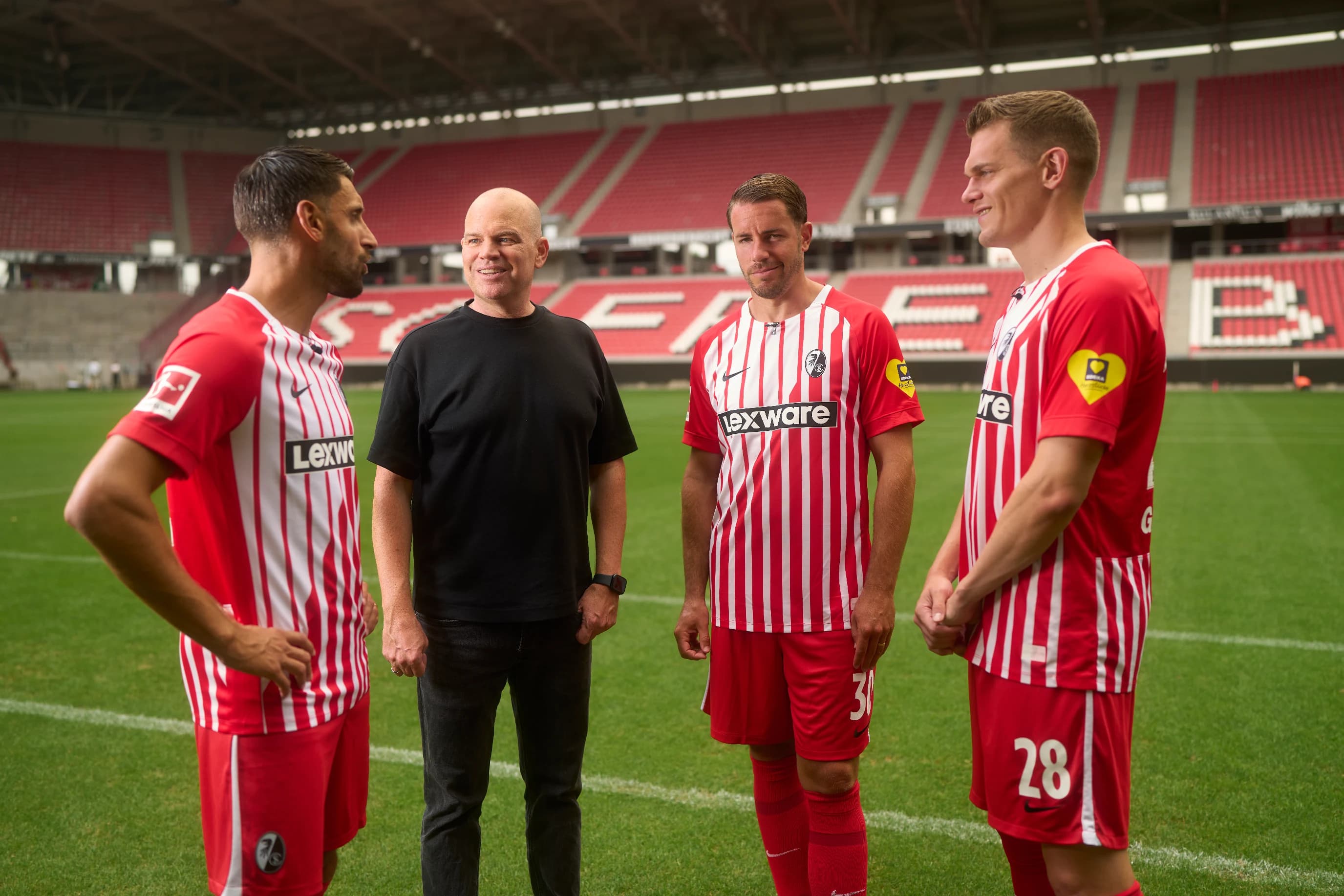 Drei Fußballspieler im SC Freiburg-Trikot und Lexware-Geschäftsführer Christian Steiger in schwarzem T-Shirt auf dem Spielfeld.