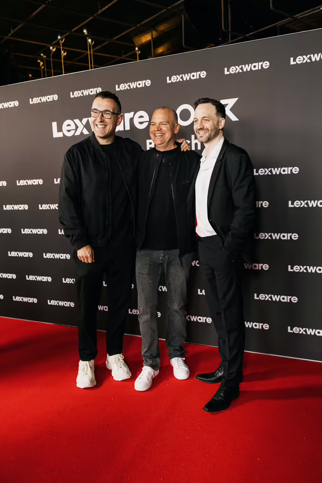 Drei Gäste posieren vor der Lexware x OMR Fotowand auf dem roten Teppich beim Founders Brunch