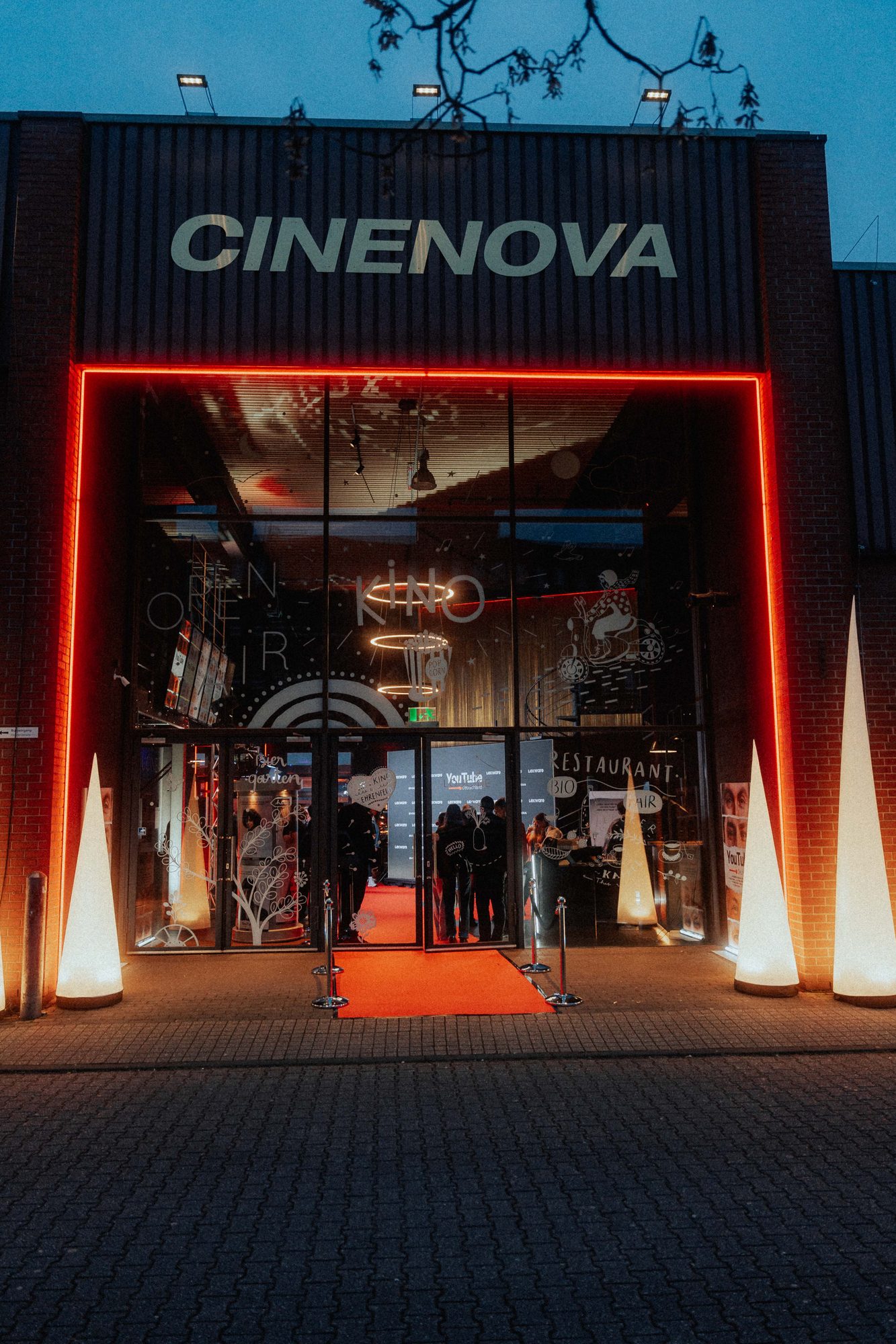 Cinenova in Köln am Abend mit leuchtendem Eingang und rotem Teppich zur Premiere von YouTube Deutschland