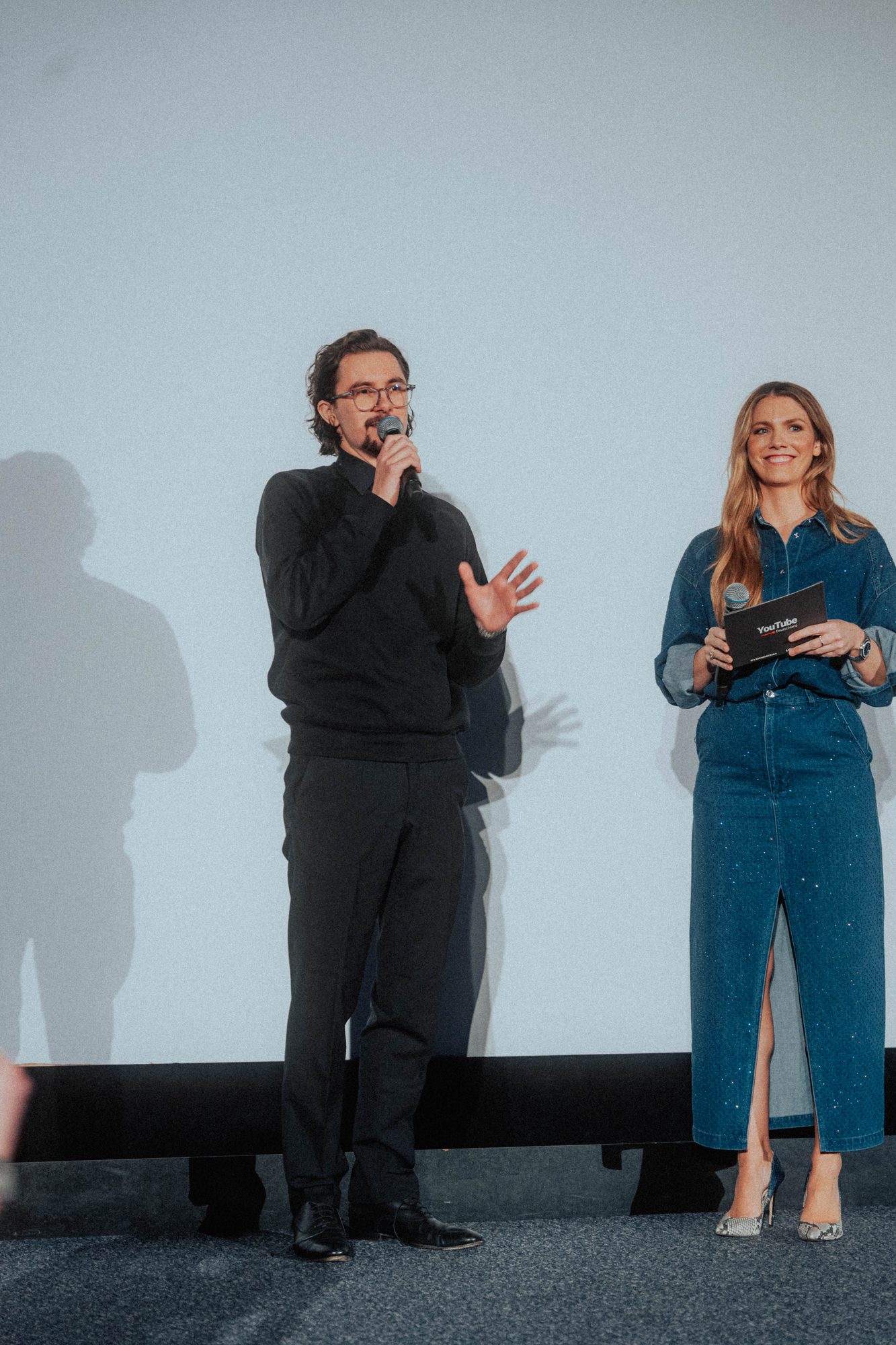 Moderatorin und Protagonist im Gespräch auf der Bühne vor der Leinwand
