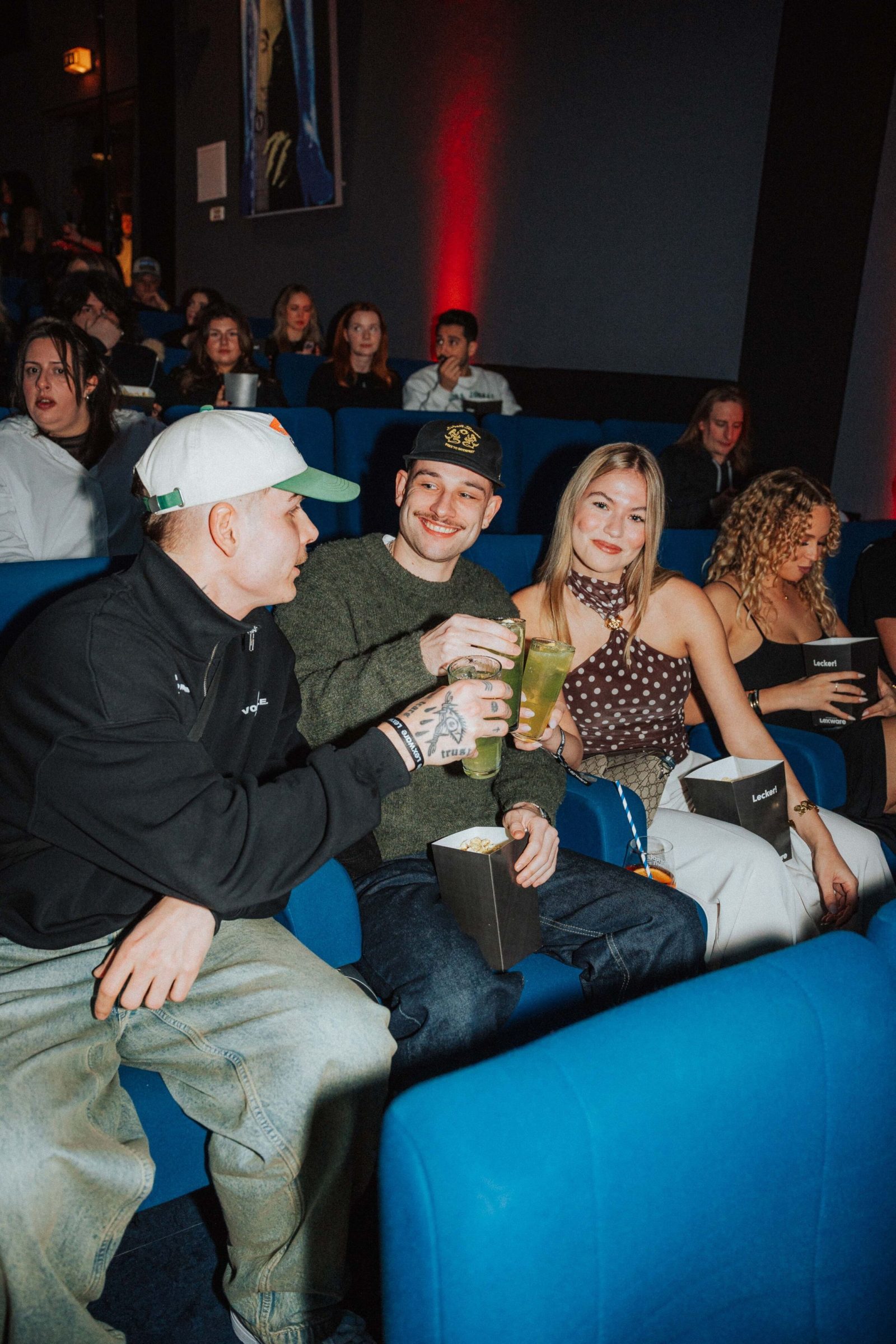Vier Gäste lachen im Kinosessel und stoßen mit Popcorn und Getränk an