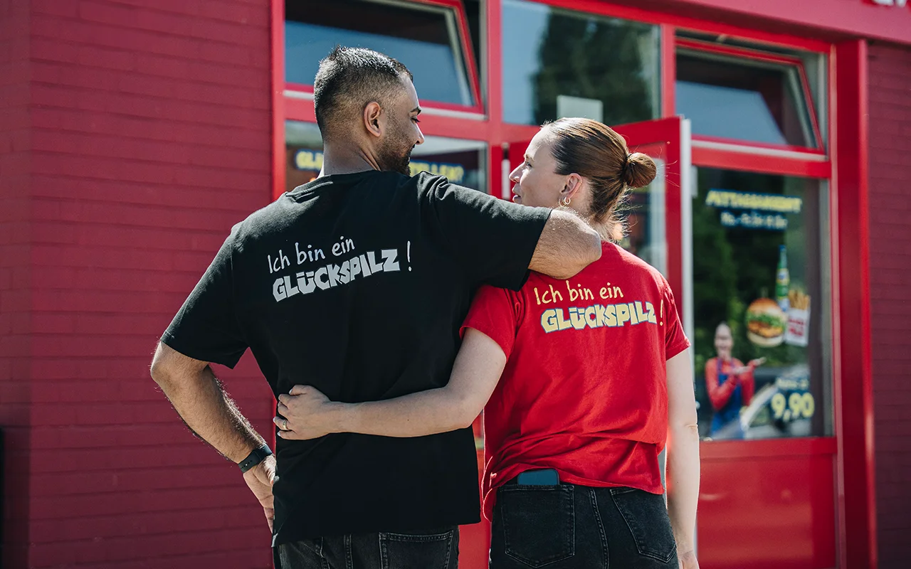 Umer Butt und seine Frau Steffi arm in arm stehen vor einer Glückspilz Filiale