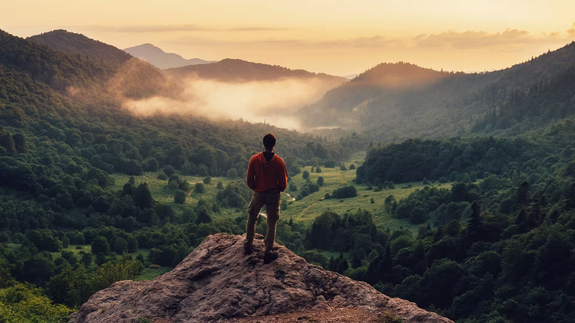 Eine Person steht auf einem Felsen umgeben von einer Berglandschaft