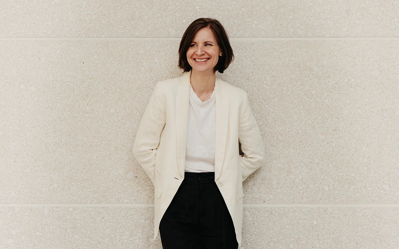 Cathy lehnt sich an einer Wand an und lächelt in die Kamera - Beitragsbild von Lexware Tell Your Story